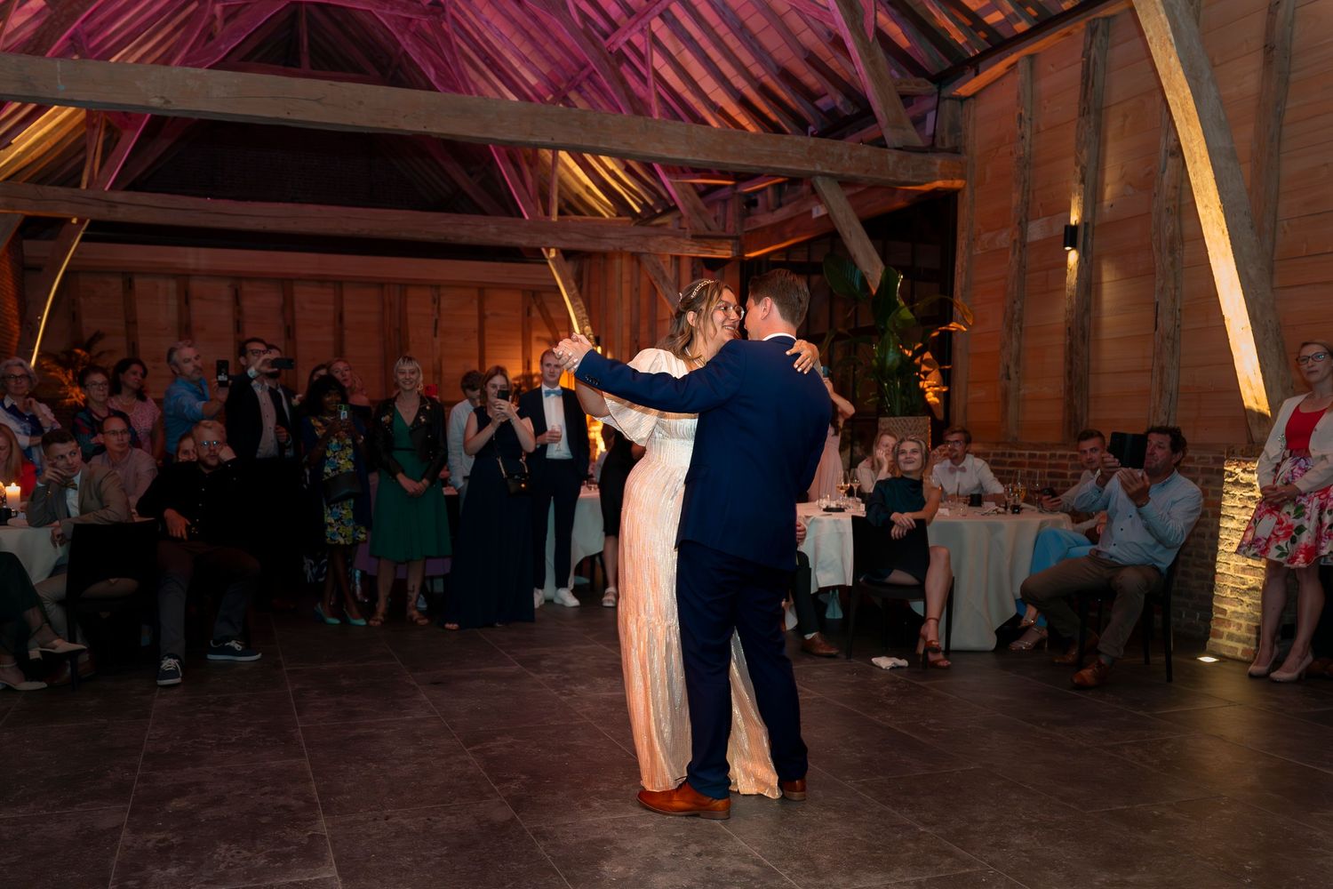 Couple dancing in spotlight during wedding reception in rustic barn venue with exposed beams.