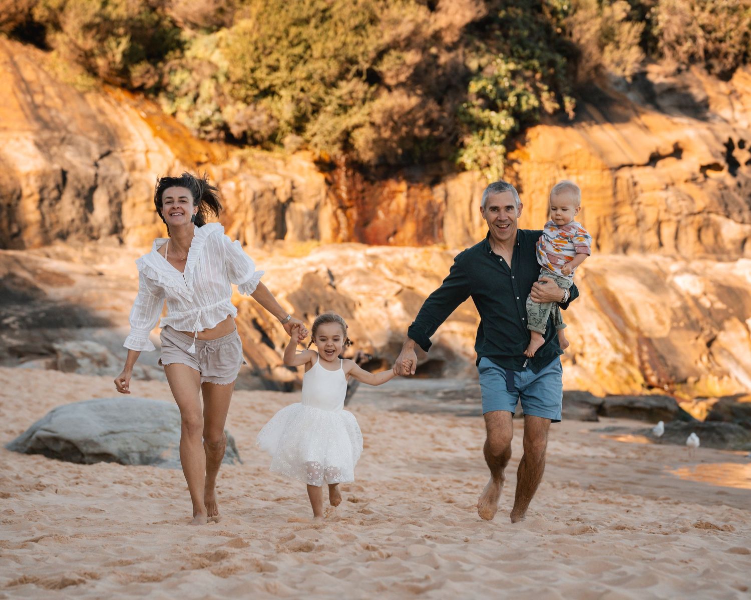 happy family running towards the camera hand in hand at the northern beaches during a family photoshoot