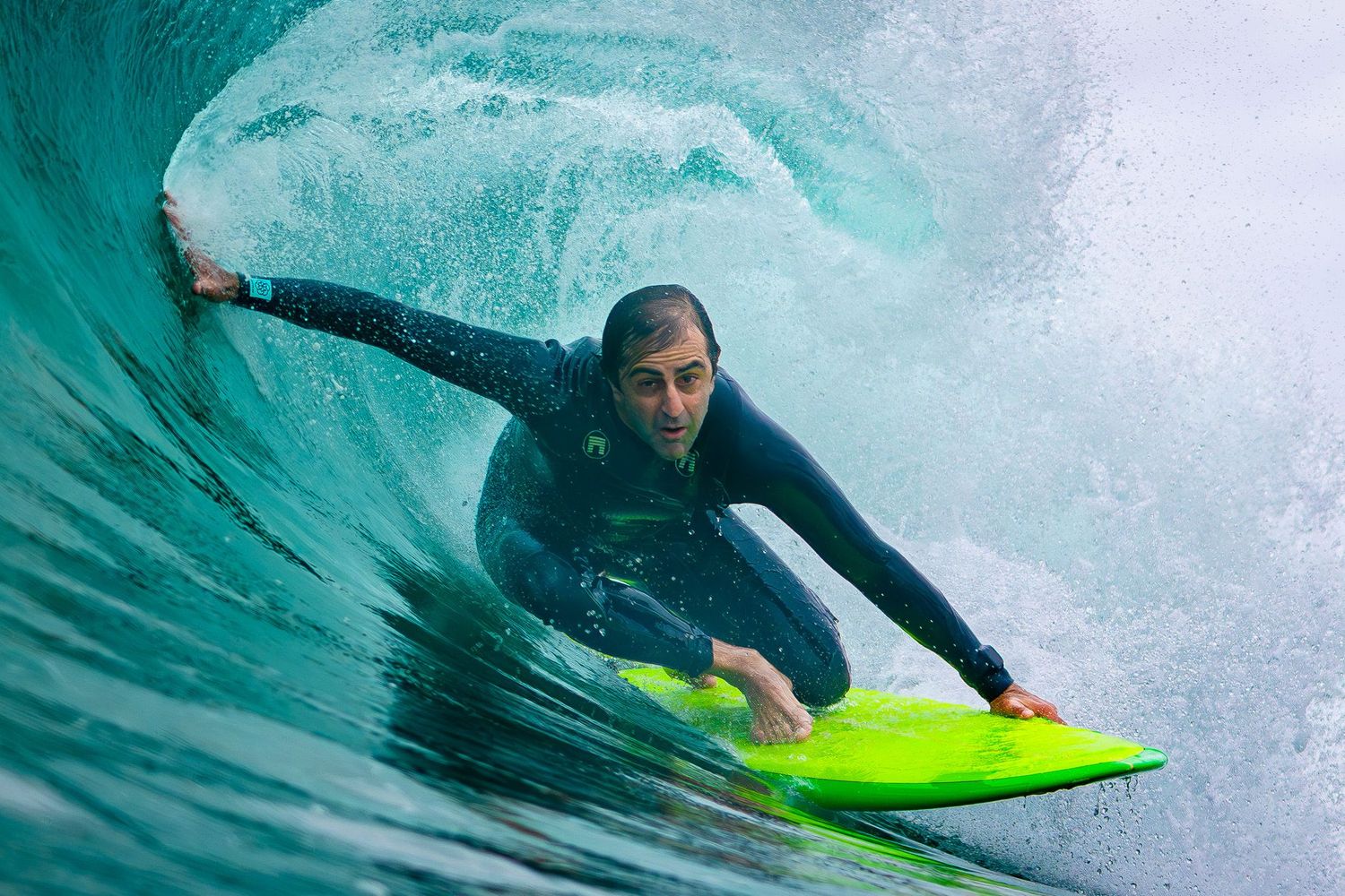San Diego surf photography of a male surfer in a wetsuit riding inside a barrel wave on a bright green surfboard.