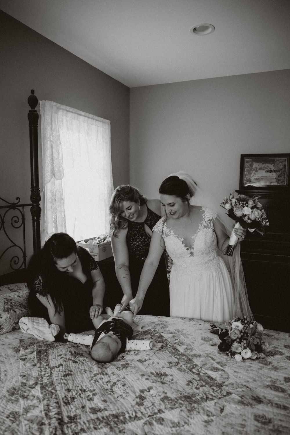 Black and white photograph showing women in formal attire preparing on a bed with floral bedspread and lace curtains in frenchtown nj.