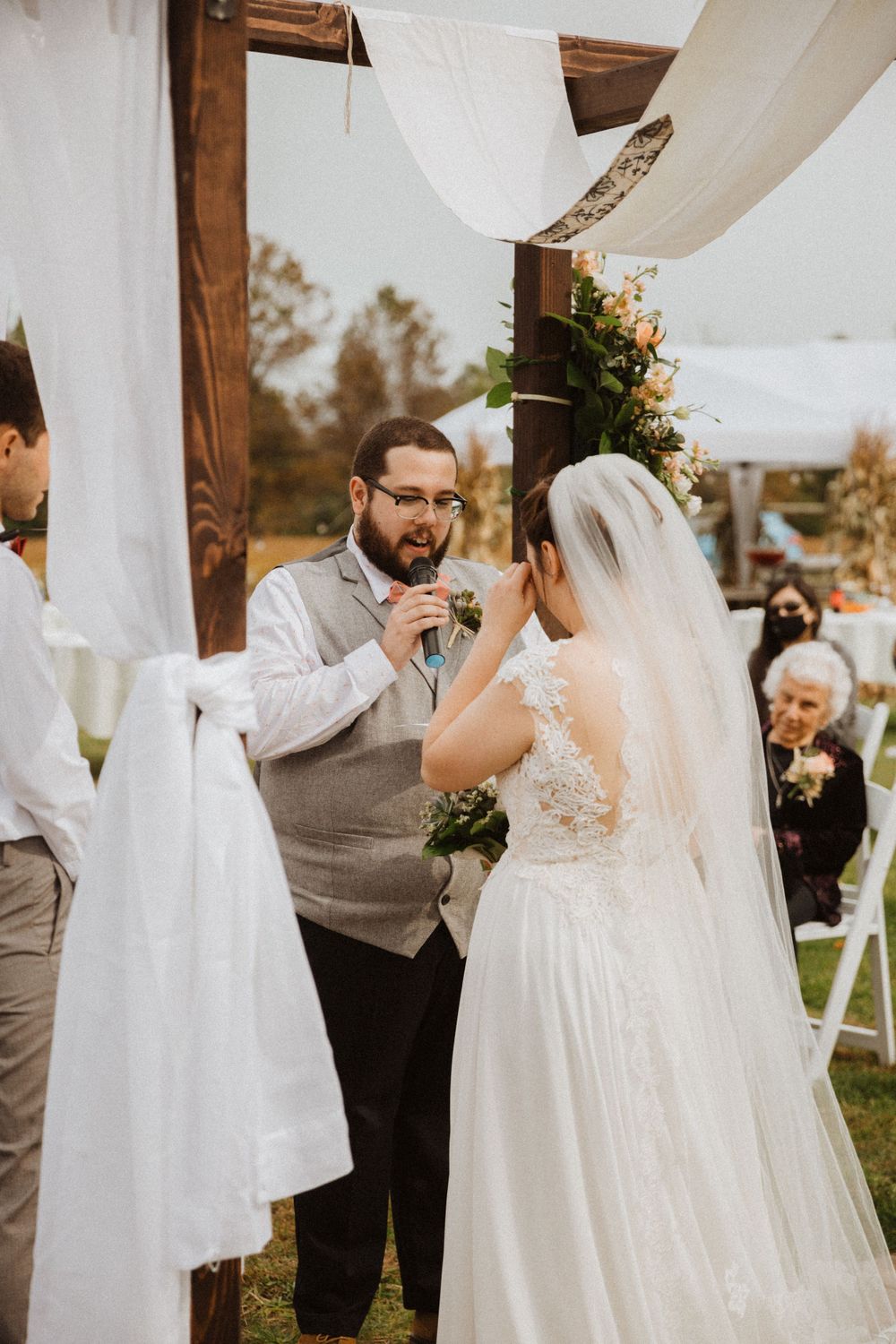 A romantic outdoor wedding ceremony under white drapes with figures exchanging vows among autumn foliage and guests in frenchtown nj.