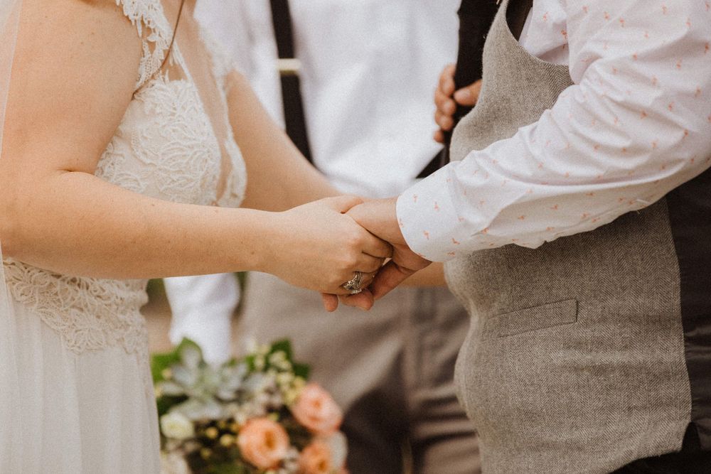 Close-up of bride and groom holding hands during wedding ceremony with peach bouquet in background in frenchtown nj.