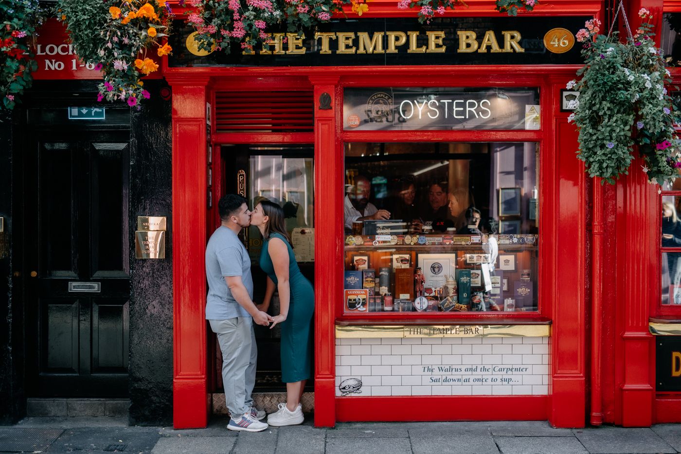 A couple stands hand in hand outside The Temple Bar, surrounded by colorful flowers and a vibrant pub entrance, sharing a tender moment.