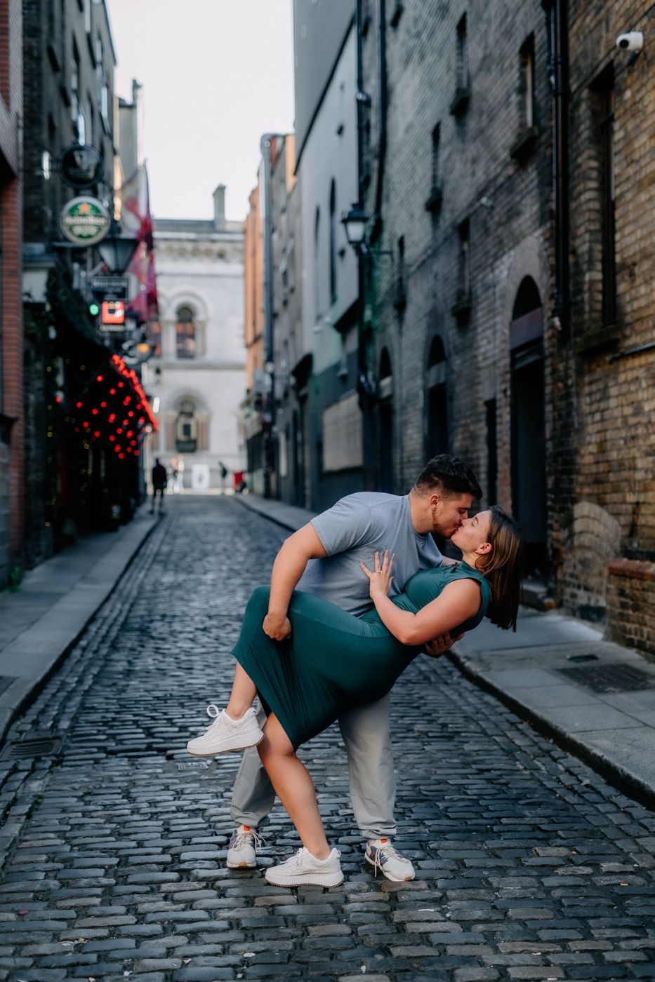 A couple embraces passionately on a cobbled street, lined with charming buildings and warm lights, capturing a romantic moment.