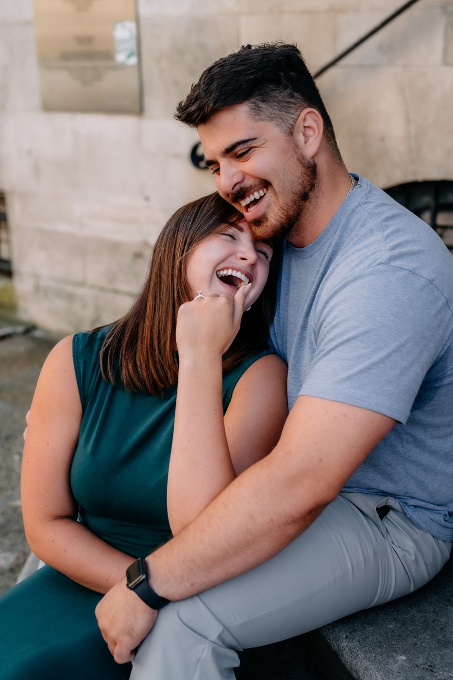 A couple sits closely on stone steps, one in a green dress and the other in a gray t-shirt, sharing an intimate moment.
