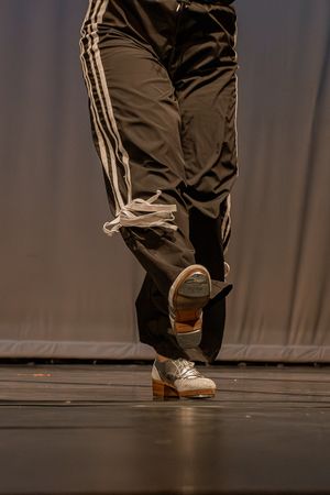 Close-up of dancer's feet wearing sneakers and Adidas track pants on dark stage.