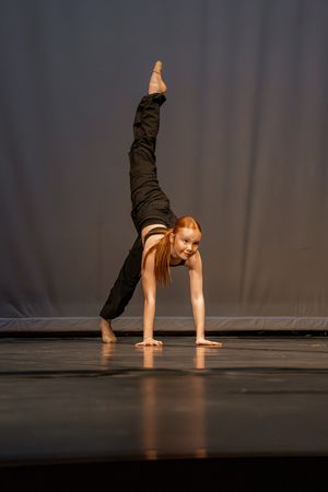 Modern dancer performs a dramatic pose with one leg extended upward on a dark stage during a contemporary performance.