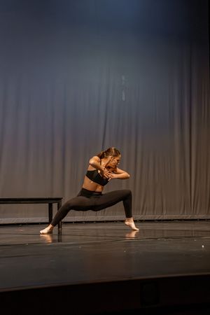 Modern dancers perform a dynamic sequence of movements across a dark stage with dramatic lighting.