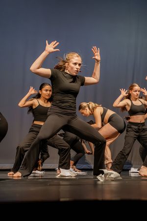 Dance ensemble performs energetic choreography in matching black outfits on stage.