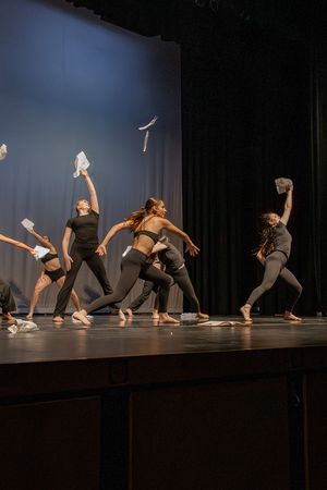 Dancers in black attire perform a dynamic contemporary routine on stage while holding white fabric props.