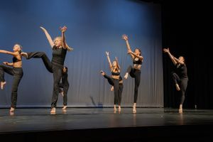 Modern dancers perform a synchronized routine in black outfits on a dimly lit stage.