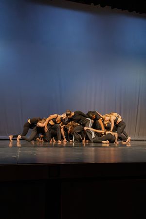 Contemporary dancers in dark clothing perform a synchronized floor routine on stage.