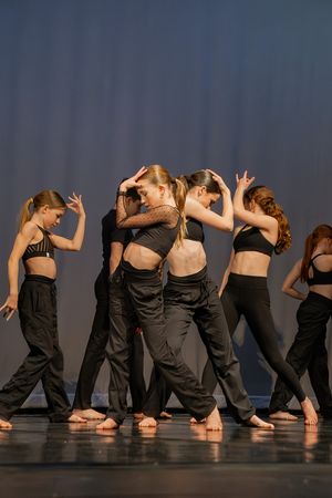 Dancers in black attire create a synchronized side-by-side formation during a contemporary performance.