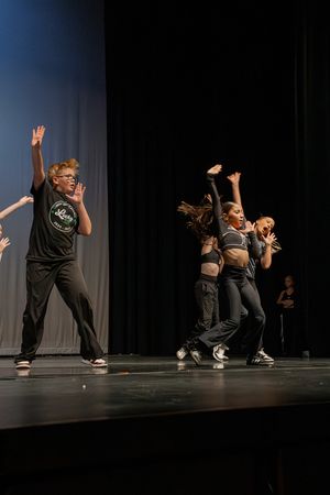Dynamic dance performance with multiple performers in black attire on dark stage.