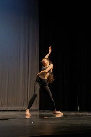 Contemporary dancer performs expressive solo movements in black attire on dark stage.