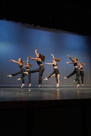 Modern dancers leap and extend in a dynamic sequence across a stage with blue lighting.
