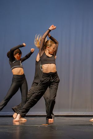 Modern dancers perform synchronized movements in black athletic wear on stage.