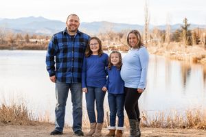 Family in coordinating blue outfits poses together by a scenic lake during golden hour.