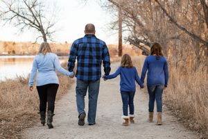 Family members walking together on a nature trail during autumn while holding hands and wearing casual clothing.