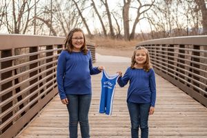 A couple in blue outfits walks hand in hand across a wooden bridge during a winter photo session.
