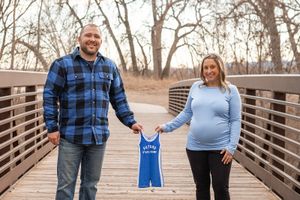 Family members in coordinated blue outfits pose playfully on a wooden bridge during a photo session.