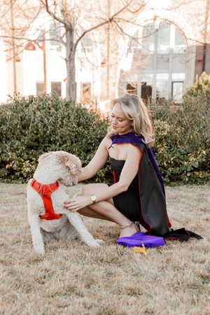 A person in black clothing stretches on brown grass with a fluffy white dog nearby.