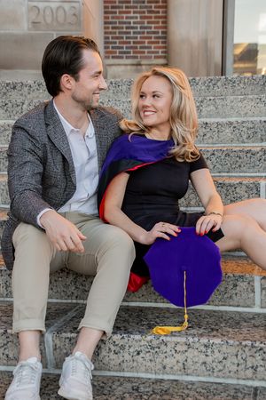 A couple sits together on concrete steps sharing a playful moment in casual attire.