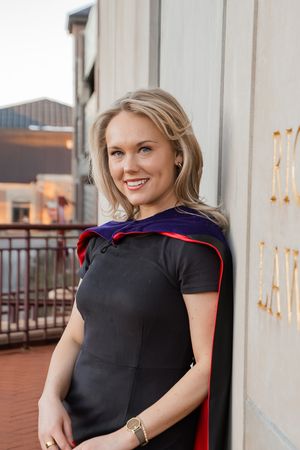 Professional headshots of a woman in a black dress and red cape posing outdoors against a light colored wall.