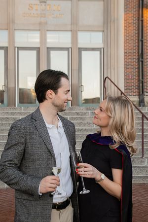 A couple in formal attire shares a romantic moment while holding wine glasses on a brick patio.