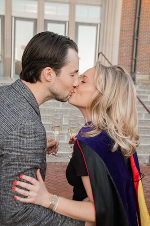 A couple shares a romantic kiss during graduation celebration outside a brick building.