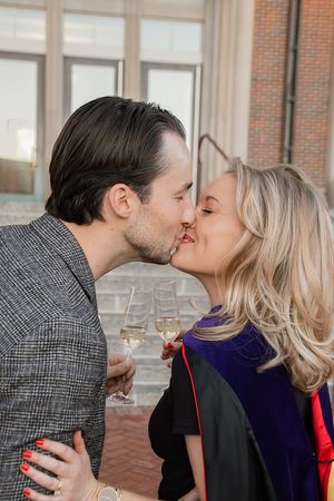 A romantic couple shares a kiss while holding wine glasses on a brick patio.
