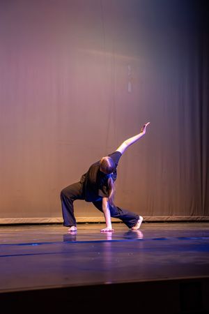 A dancer performs a graceful contemporary dance sequence in a dark theater with dramatic purple lighting.