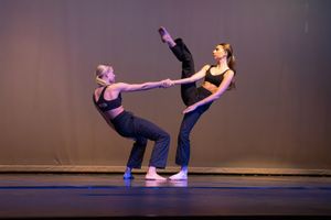 Dancers perform a series of graceful contemporary dance movements on a dimly lit stage in matching black outfits.