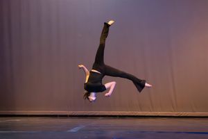 A dancer performs a graceful split leap against a dark background, creating a dynamic silhouette.