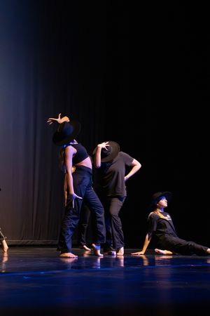 Modern dancers perform on a dark stage with dramatic lighting, striking expressive poses during a contemporary dance piece.