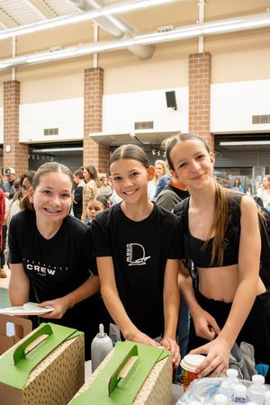 A group wearing black shirts leans over a green surface while participating in an indoor activity.