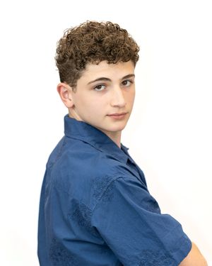 Young teen boy with curly brown hair wearing a blue button-up shirt poses for a portrait photo.