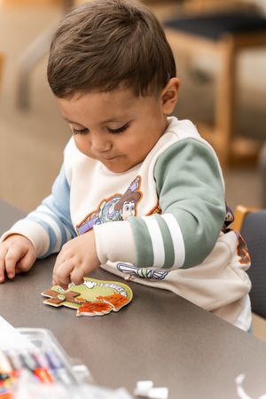 Toddler in Toy Story hoodie playing with colorful stickers at a table.