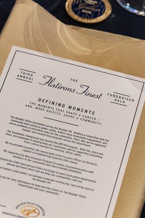 Printed program for the Third Annual Flatirons Finest fundraiser gala by the Boulder Police Foundation, resting on a gold table linen.