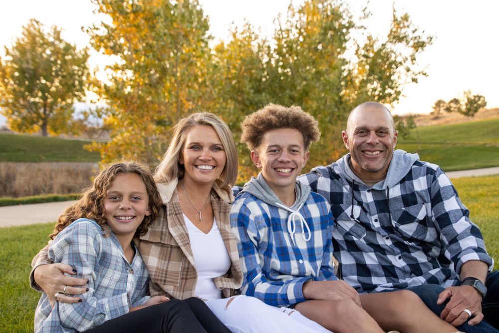 Family in matching plaid shirts sitting together on grass during golden hour.