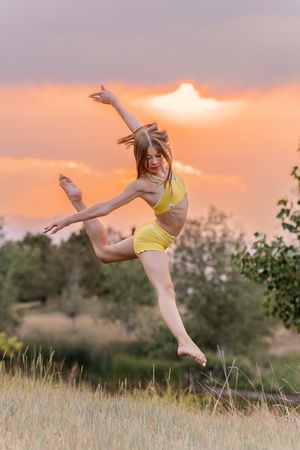 Athletic girl leaps gracefully at sunset in yellow crop top and shorts against colorful sky.