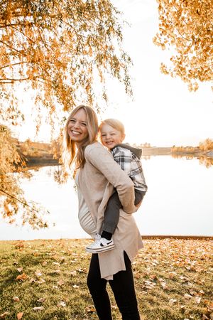 Two people share joyful moments under golden autumn trees by a lake during sunset.