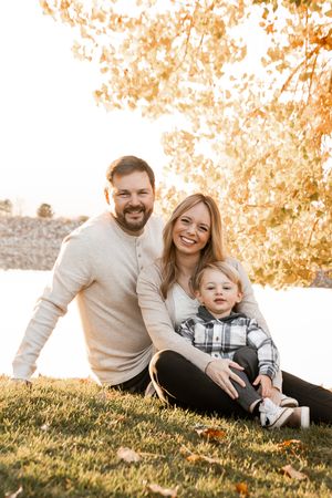 A family sits together on a grassy hill during golden hour, sharing joyful moments in autumn light.