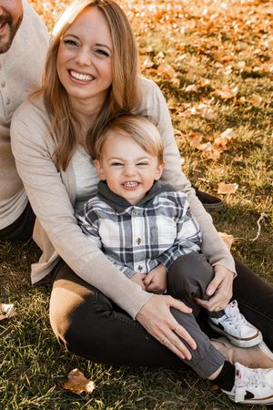 A joyful autumn family moment captured in warm sunlight with fallen leaves on the grass.