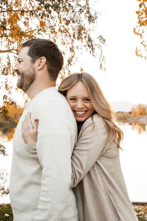 A couple embraces and laughs together during a romantic autumn photoshoot with golden trees in the background.