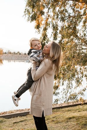 A playful autumn moment captured by a lake with falling leaves and golden sunlight filtering through branches.