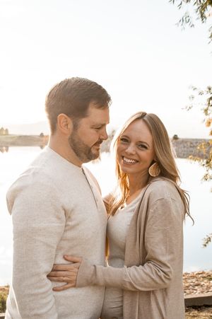 A couple shares joyful laughter together during a romantic sunset photoshoot outdoors in neutral-toned clothing.