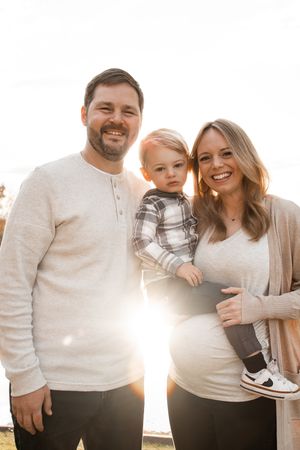 Family wearing matching cream sweaters poses together outdoors during golden hour sunset.
