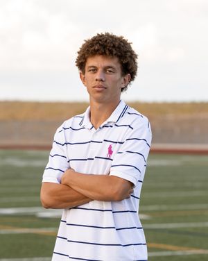 Teen boy in striped Ralph Lauren polo with arms crossed on athletic field.