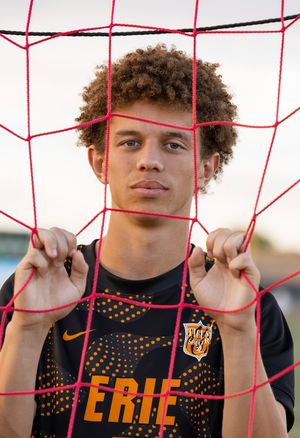 Young soccer player in Erie jersey holds pink goal net, looking confidently at camera on outdoor field.